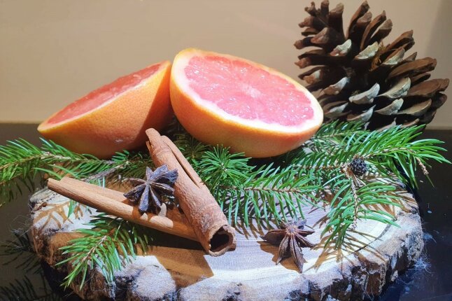 Halbierte Grapefruit, Zimtstange, Sternanis und Tannennadeln auf einem Holzbrett