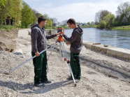 Ausbilder erläutert dem Auszubildenden die Verwendung eines Nivelliergerätes zum Vermessen einer Pflasterfläche