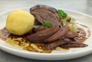 Entenbraten mit Kartoffelknödel und Portweinschalotten auf einem Teller.