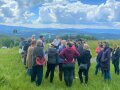 Viele Teilnehmer inmitten grüner Wiese mit den Bayerwaldbergen im Hintergrund als Panorama