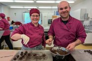 Zwei Studierende tauchen Pralinen in Kuvertüre und rollen sie auf einem Gitter ab.