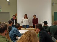 Es erfolgt die Begrüßung der Teilnehmer vor der Tafel im Klassenzimmer