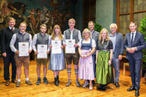 Die Absolventen stehen im Prunksaal mit ihren Urkunden und den Ehrengästen.